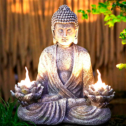Estatueta do Buda meditando iluminado por velas nas mãos cujo suporte tem formato floral